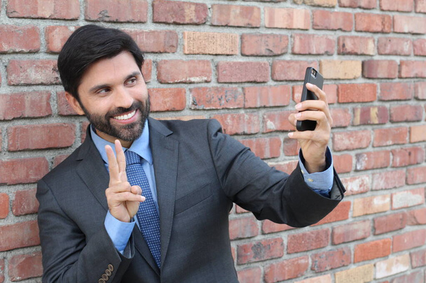 Young businessman taking a selfie with his smartphone on brick wall background  - Photo, Image