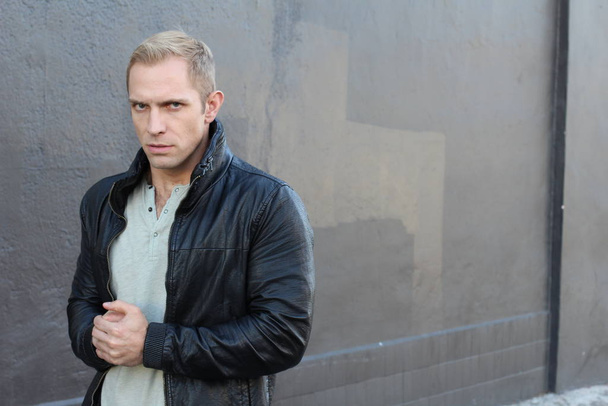 close-up shot of handsome adult man in leather jacket in front of dark grey wall on street - Photo, Image