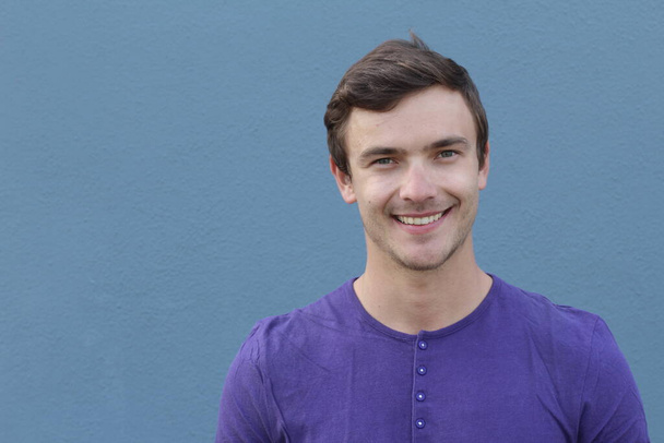 close-up portrait of handsome young man in purple shirt in front of blue wall - Photo, Image