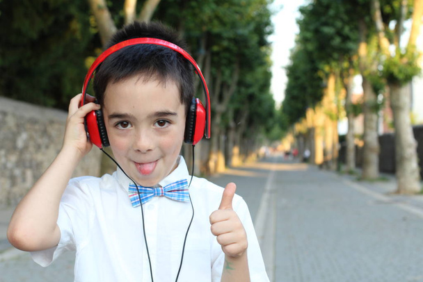 屋外に立つ赤いヘッドフォンでスタイリッシュな子供の男の子のクローズアップ肖像  - 写真・画像