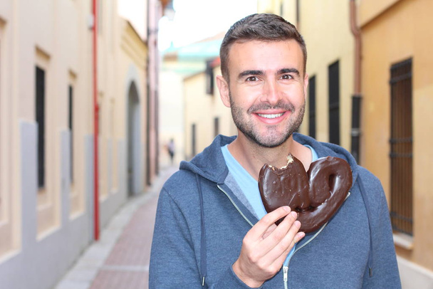 Homem comendo uma massa de chocolate sopro em forma de coração
 - Foto, Imagem