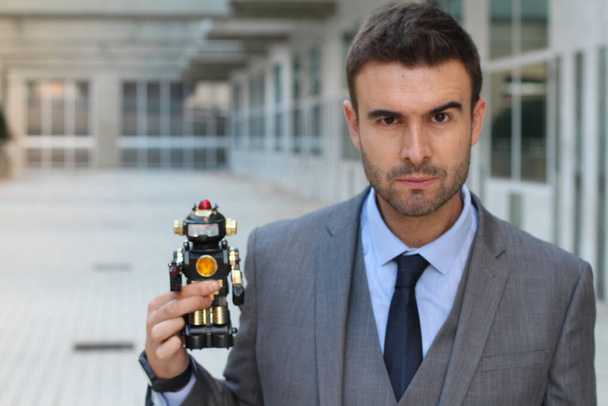 primer plano de joven hombre de negocios guapo en traje gris sosteniendo figura robot de juguete en la calle
 - Foto, Imagen