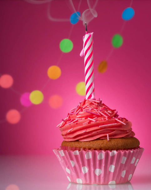 cupcake festif avec bougie et crème sur fond rose décoré de confettis colorés
 - Photo, image