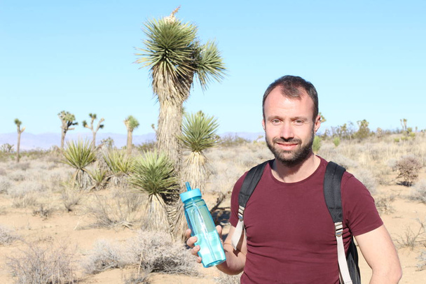 zblízka portrét pohledného mladého muže s batohem a plastovou sportovní láhev v poušti - Fotografie, Obrázek