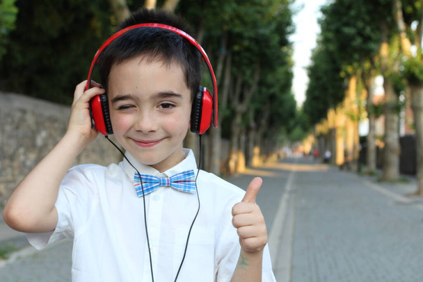 Portrait en gros plan d'un enfant garçon élégant dans des écouteurs rouges se tenant debout à l'extérieur  - Photo, image