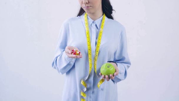 обрізаний вид жінки, що порівнює вітаміни та яблуко, ізольовані на білому
 - Кадри, відео