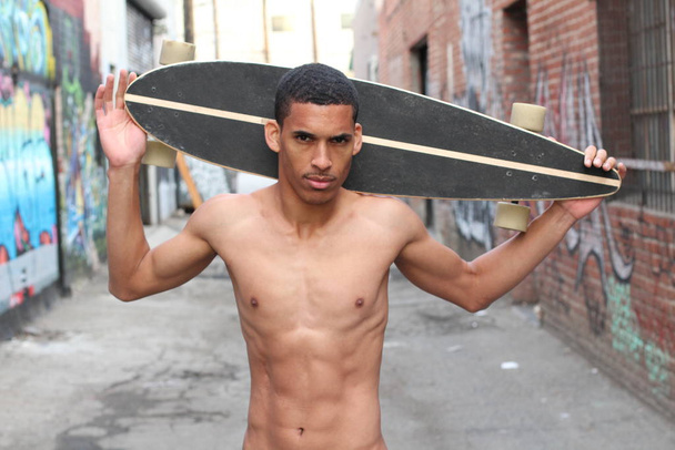 close-up portrait of handsome young shirtless african american man with longboard on street - Photo, Image