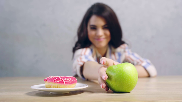 selektywne skupienie się kobiety wybierającej między jabłkiem a pączkiem  - Materiał filmowy, wideo