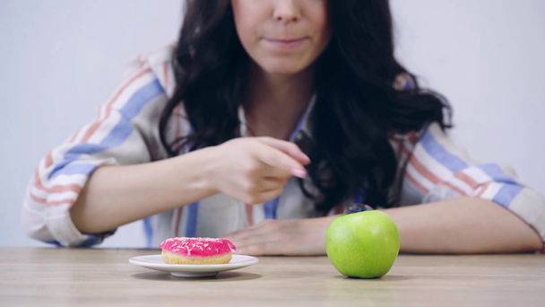 oříznutý pohled na dívku vybírající mezi jablkem a koblihou  - Záběry, video