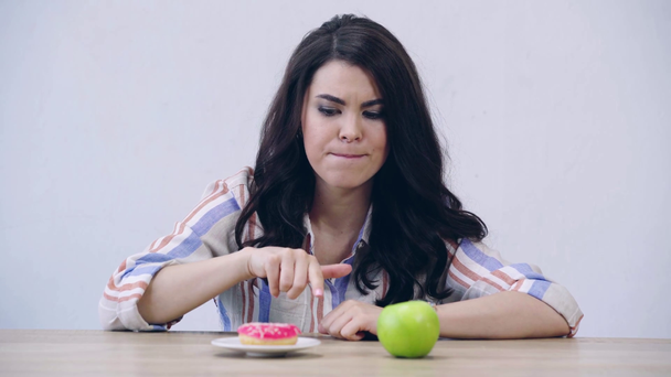mylić dziewczyna wybierając między jabłkiem i pączkiem - Materiał filmowy, wideo
