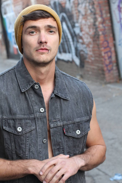 close-up portrait of handsome young man in stylish denim vest and yellow hat on street - Photo, Image