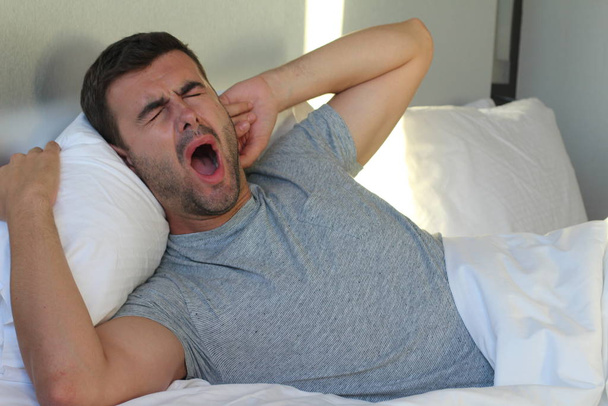 крупным планом портрет красивого молодого человека, зевающего в постели дома - Фото, изображение