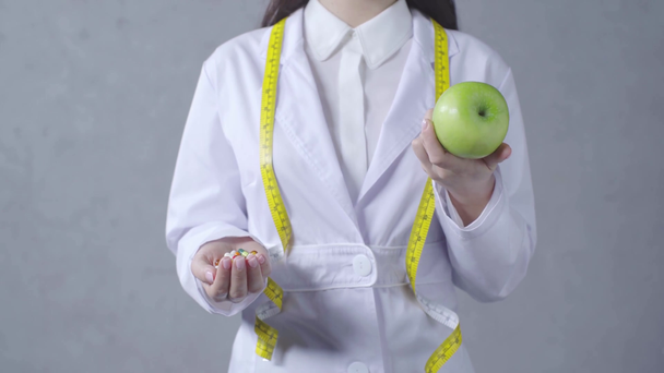 обрезанный взгляд диетолога, сравнивающего яблоко и витамины на сером
 - Кадры, видео