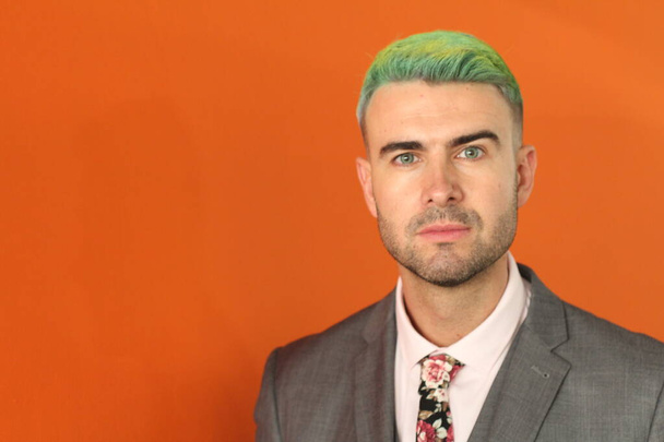 Elegante knappe man met groen haar op oranje achtergrond - Foto, afbeelding