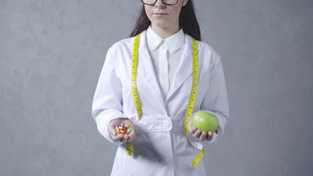 bijgesneden weergave van arts kiezen tussen appel en vitaminen op grijs - Video