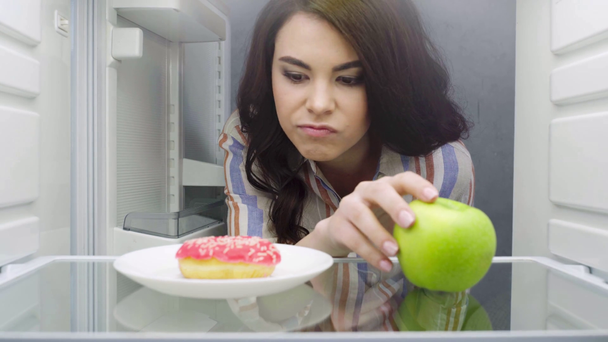 attractive girl taking doughnut from fridge - Footage, Video