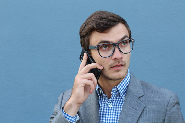 青い壁の前で電話で話しているハンサムな若いビジネスマンのクローズアップ肖像画 - 写真・画像