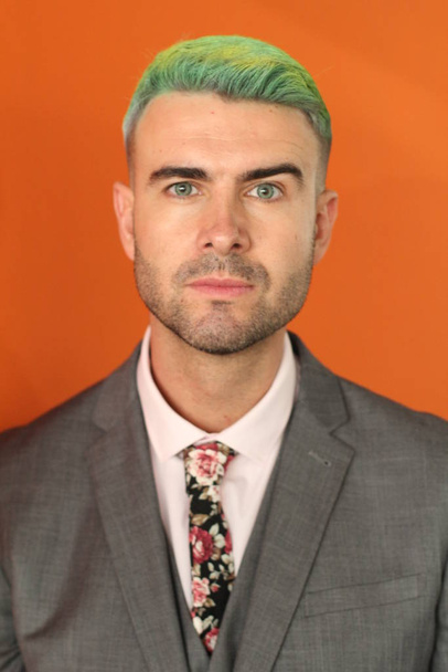 Elegant handsome man with green hair standing on orange background - Foto, afbeelding
