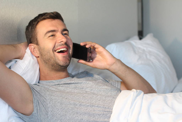close-up portrait of handsome young man talking by phone in bed at home - Valokuva, kuva