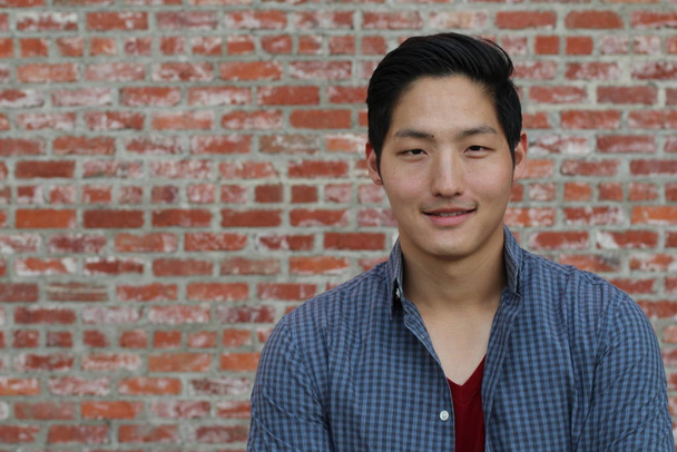 close-up portrait of handsome young asian man in casual clothes in front of brick wall - Photo, Image
