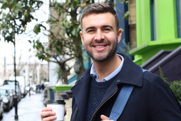 close-up portrait of handsome young man in warm coat on street with paper cup of coffee - Foto, Imagen