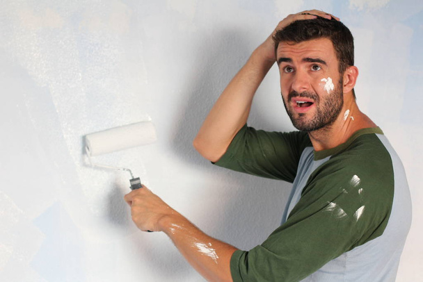close-up retrato de bonito jovem homem pintura parede com rolando escova em casa
 - Foto, Imagem