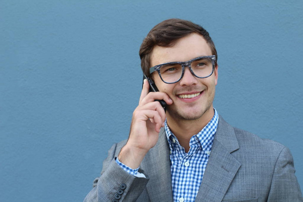 κοντινό πορτραίτο όμορφου νεαρού επιχειρηματία που μιλάει τηλεφωνικά μπροστά στον μπλε τοίχο - Φωτογραφία, εικόνα