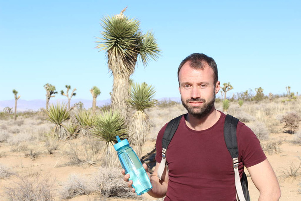 retrato de cerca del joven guapo con mochila y botella de plástico en el desierto
 - Foto, imagen