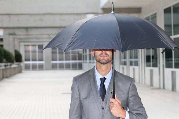 Businessman hiding under an umbrella in office space - Foto, imagen