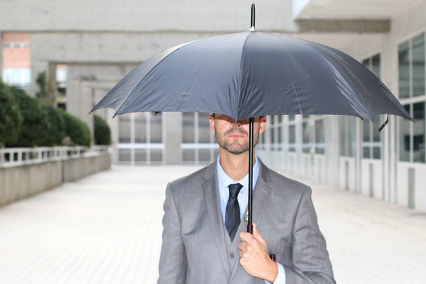 Businessman hiding under an umbrella in office space - Photo, Image