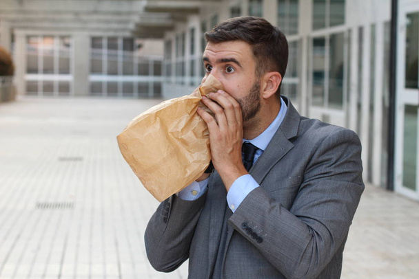 close-up portrait of stressed young businessman breathing with paper bag - Fotó, kép