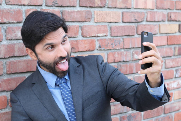 Молодой бизнесмен делает селфи со своим смартфоном на фоне кирпичной стены
  - Фото, изображение