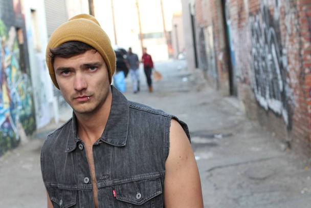 Nahaufnahme Porträt eines hübschen jungen Mannes in stylischer Jeansweste und gelbem Hut auf der Straße - Foto, Bild