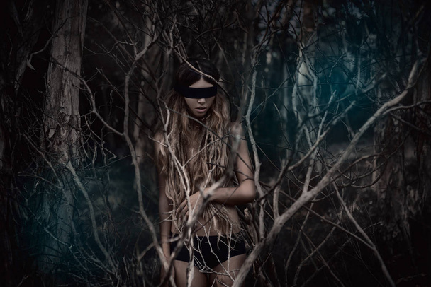 Young beautiful blindfolded woman in dark spooky forest - Fotoğraf, Görsel