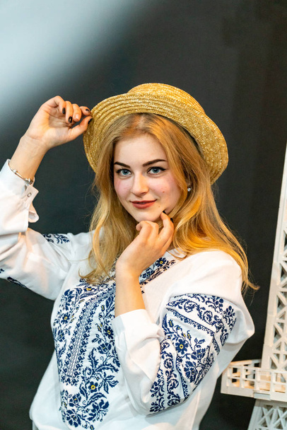 fiatal nő visel fonott kalap és hímzett ing pózol stúdióban - Fotó, kép