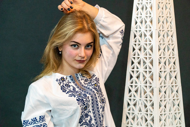 blond mooi vrouw poseren in studio door decoratie in geborduurd shirt - Foto, afbeelding