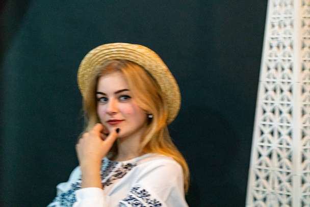 młoda kobieta w wiklinowym kapeluszu i haftowanej koszuli pozowanie w studio - Zdjęcie, obraz