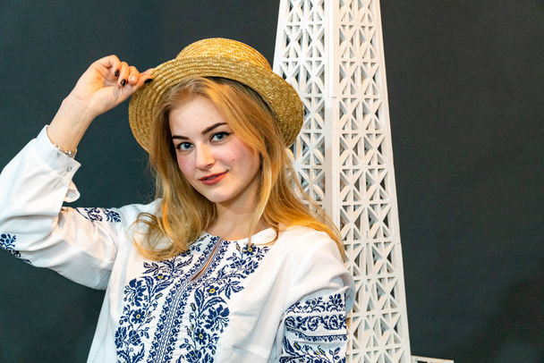 молодая женщина в плетеной шляпе и вышитой рубашке позирует в студии - Фото, изображение