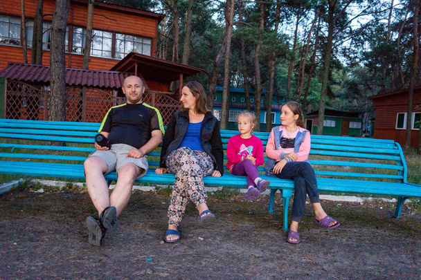 Οι γονείς και οι κόρες της κάθονται στον πάγκο στο πάρκο. - Φωτογραφία, εικόνα