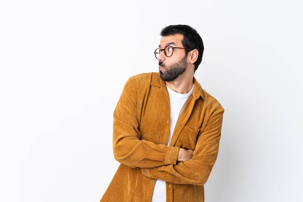 Caucasian handsome man with beard wearing a corduroy jacket over isolated white background making doubts gesture looking side - Photo, image