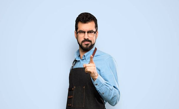 Man with apron frustrated and pointing to the front over isolated blue background - Fotoğraf, Görsel