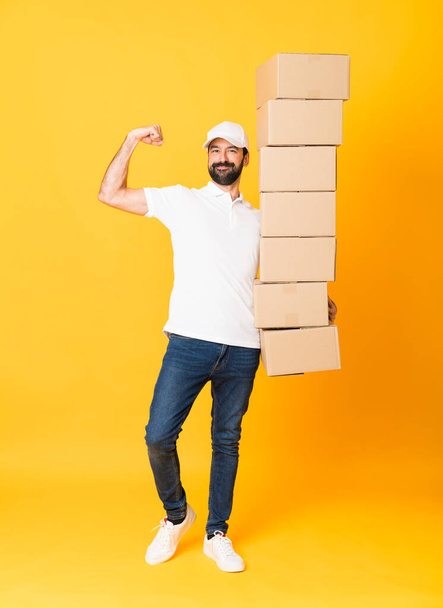 Full-length shot of delivery man among boxes over isolated yellow background - Фото, изображение