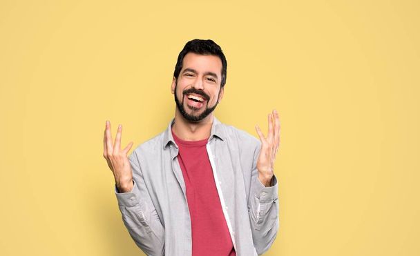 Handsome man with beard smiling a lot over isolated yellow background - Photo, image