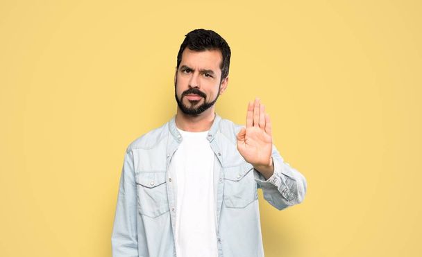 schöner Mann mit Bart macht Stop-Geste vor isoliertem gelben Hintergrund - Foto, Bild