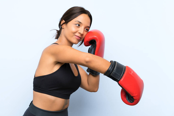 Mladá sportovní dívka s boxerskými rukavicemi přes izolované modré pozadí - Fotografie, Obrázek