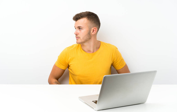 Jeune homme blonde dans une table avec un ordinateur portable côté regardant
 - Photo, image