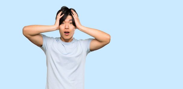 Asian man with blue shirt with surprise expression over isolated blue background - 写真・画像