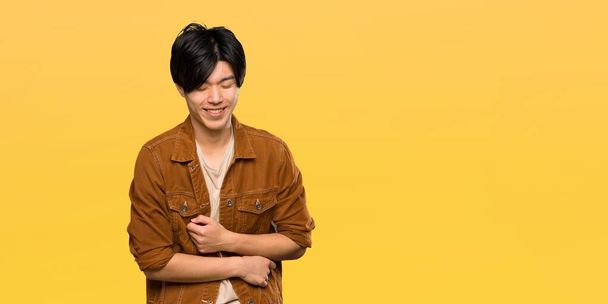 Azjatycki człowiek z brązową kurtkę uśmiechnięty dużo ponad białym tle żółty - Zdjęcie, obraz
