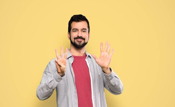 Beau homme avec barbe comptant huit doigts sur fond jaune isolé
 - Photo, image
