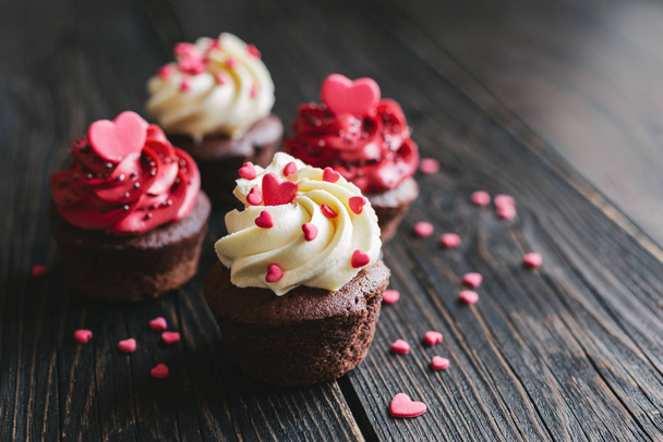 白と赤のバレンタインカップケーキ,暗い木製のテーブルの上に甘い心で飾られた.  - 写真・画像